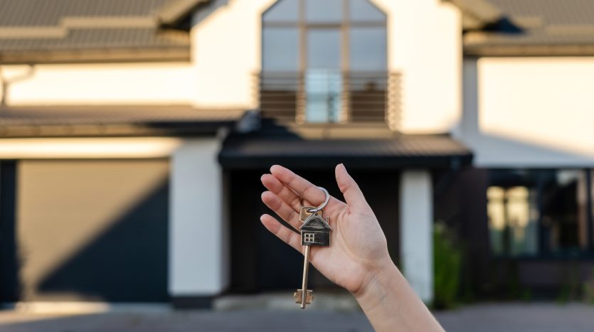 Mano di una ragazza con delle chiavi in mano davanti a una casa